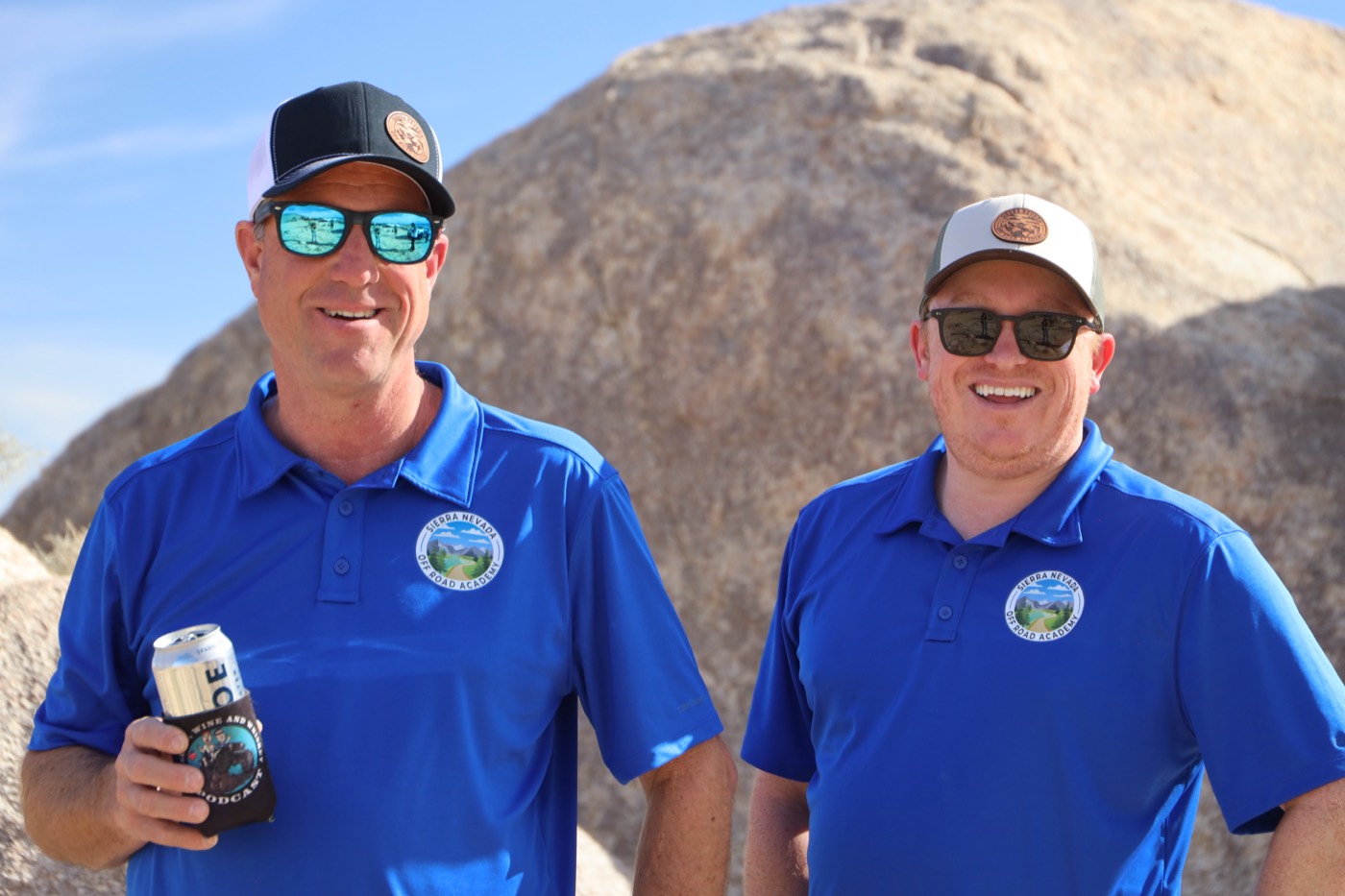 CJ Arnesen (right) with his Sierra Nevada Off Road Academy co-founder, both in branded polos, in front of a large granite boulder in the high desert.